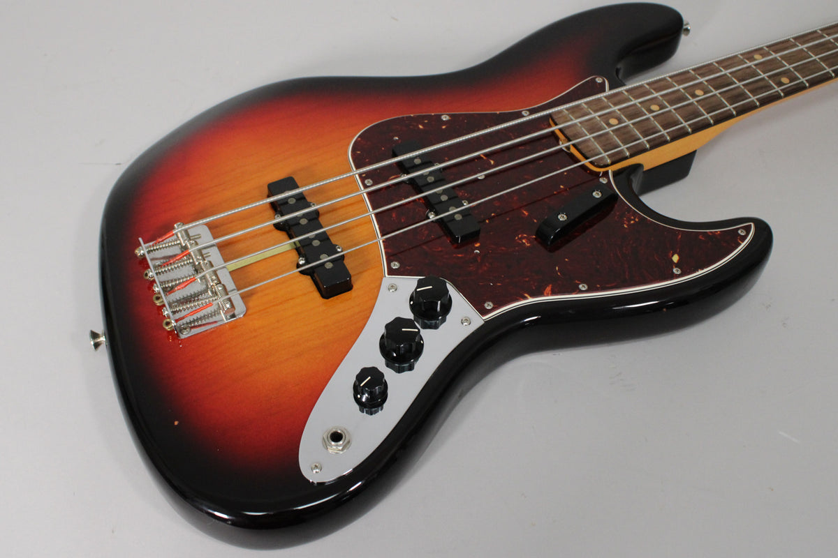 The sunburst bass body is angled from the lower left, showing the chrome bridge, two black pickups, tortoise pickguard, and control plate.