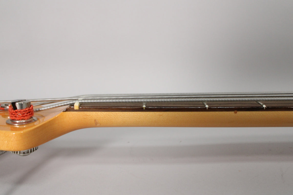 Close-up of the bass neck from the side, showing the light-colored maple neck, dark fretboard, nut, and strings.