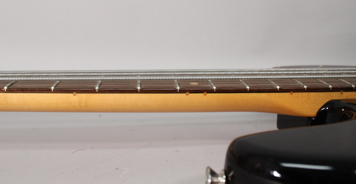Close-up of the bass neck from the side, showing the dark fretboard, light maple neck, and a few small dings.