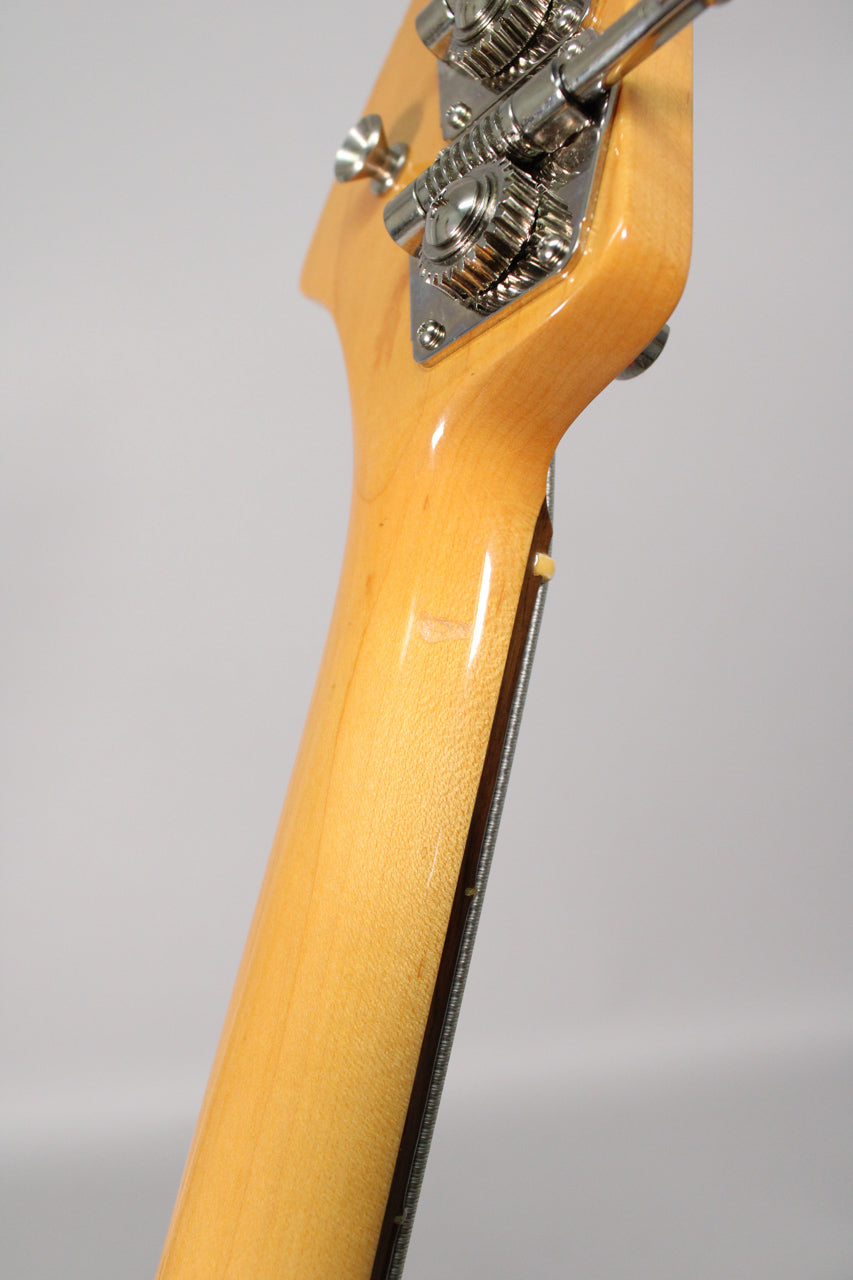 Close-up of the bass's glossy amber-finished neck and headstock from behind, showing chrome tuners and a small ding on the neck.