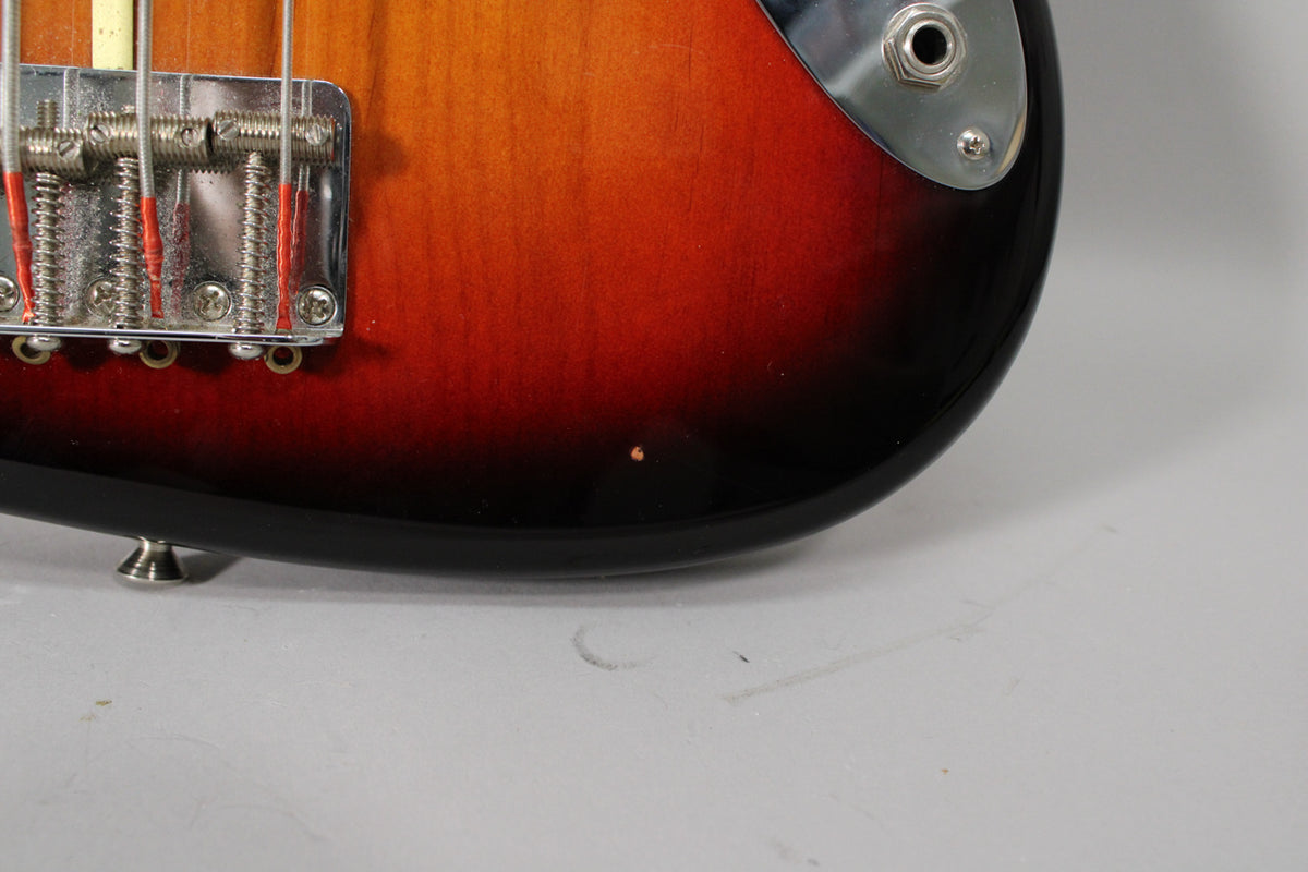 Close-up of the bass body's lower bout, showing the chrome bridge, output jack, strap button, and a small ding in the sunburst finish.