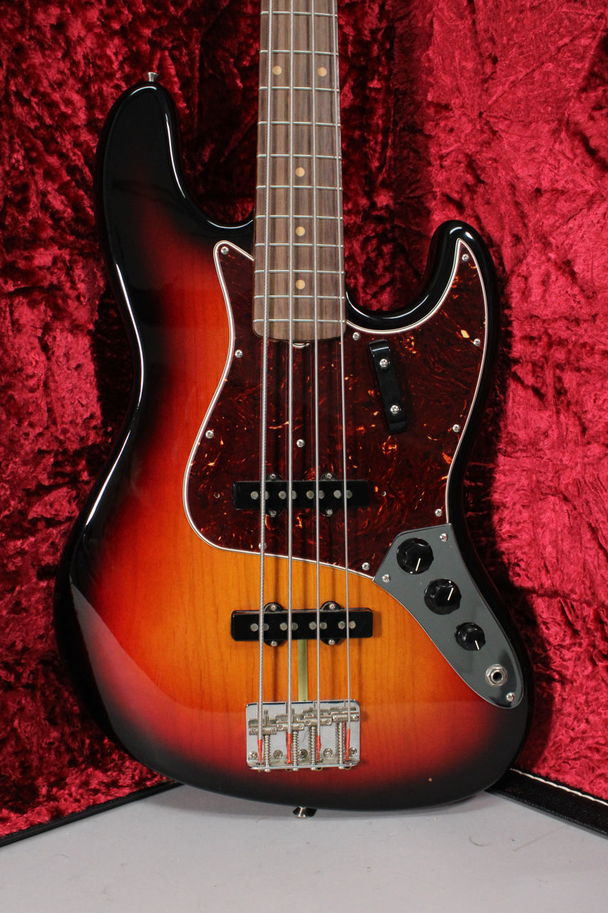 A 3-color sunburst Jazz Bass, angled slightly, showing the body, neck, and headstock against a red velvet case lining.