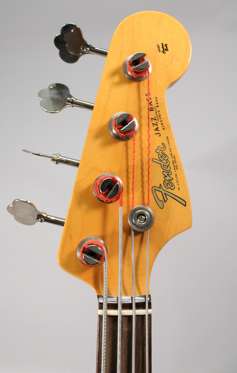 Close-up of the bass headstock, showing the light amber finish, four chrome clover-leaf tuners, and a round string tree.