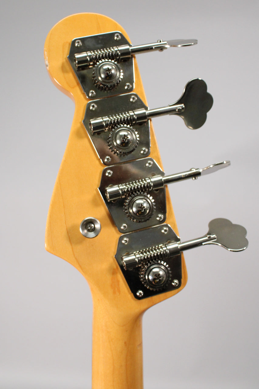 The back of the bass headstock, showing four chrome clover-leaf tuners on a light wood finish, with a small ding near the top.
