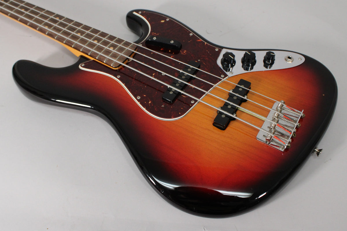 The sunburst bass is angled from the upper left, showing its glossy body, tortoiseshell pickguard, and chrome bridge and controls.