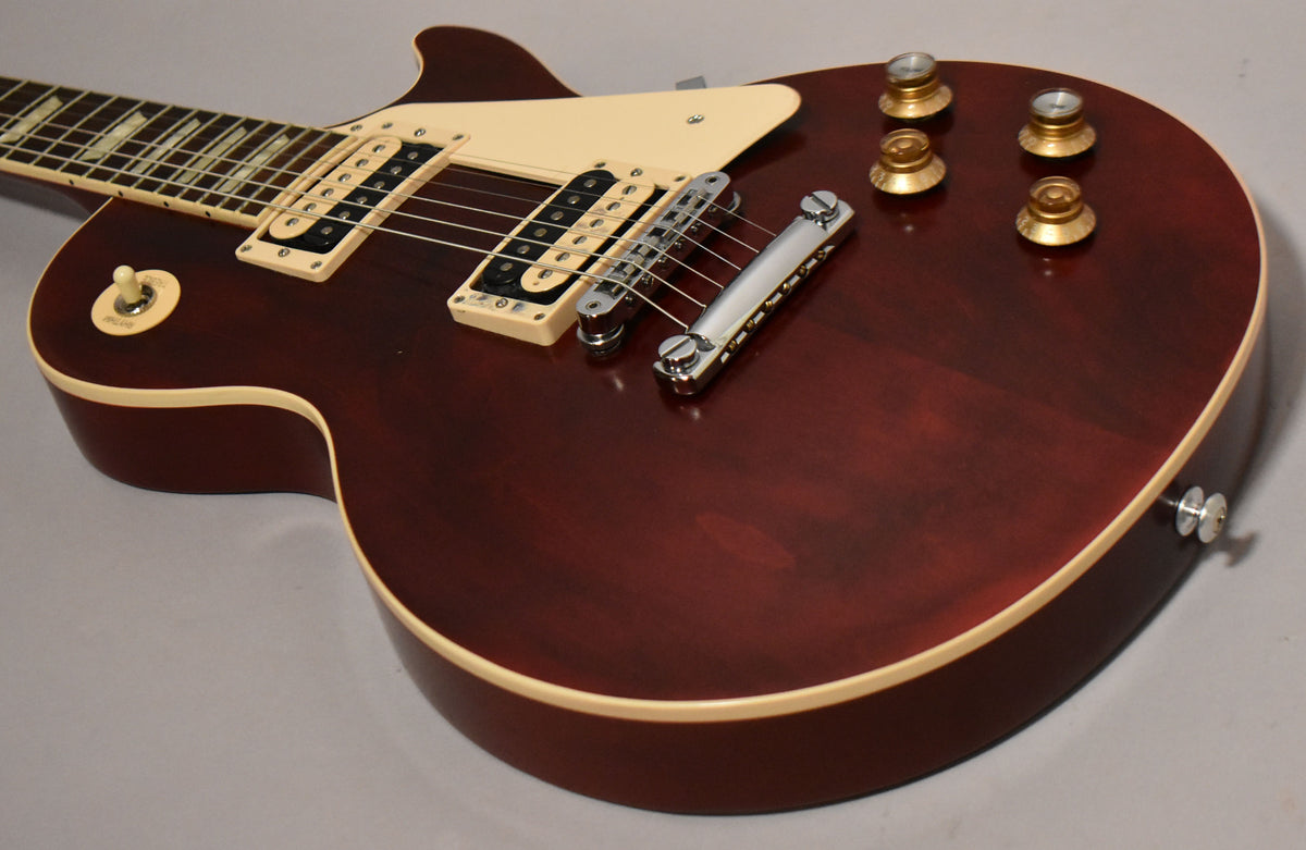 The wine red body with cream binding is angled, showing the neck, two cream humbuckers, chrome bridge, and four gold knobs.