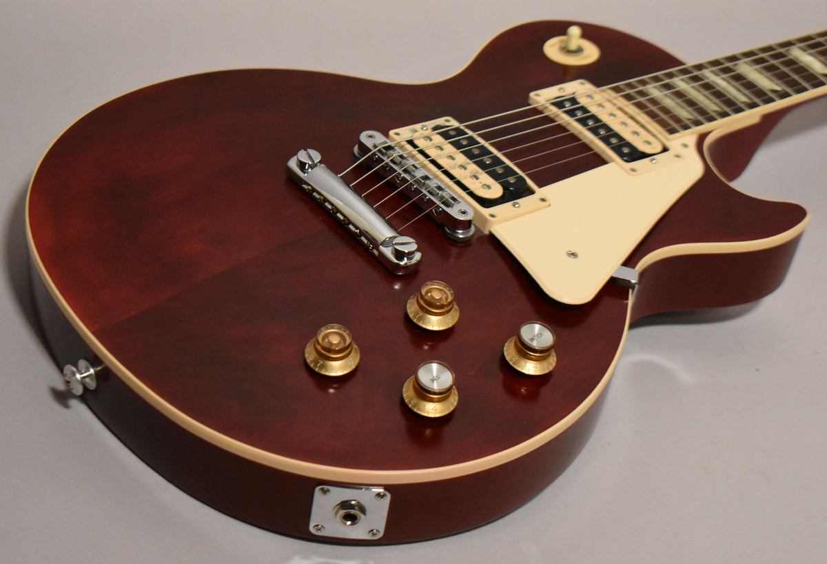 Upper body of a wine red Les Paul, showing cream binding, humbuckers, pickguard, chrome bridge, and four gold top hat knobs.