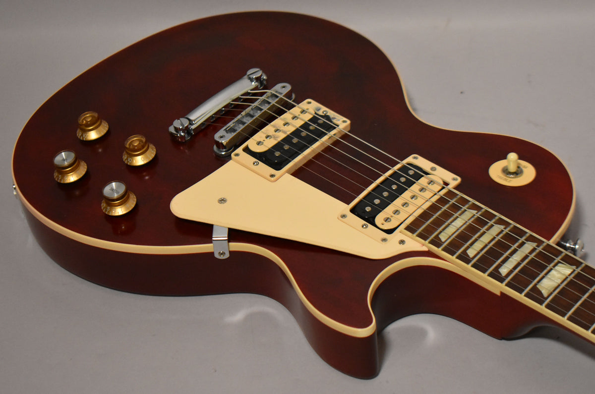 The wine red Les Paul body, with cream binding and pickguard, is angled to show the gold top hat knobs and humbucker pickups.