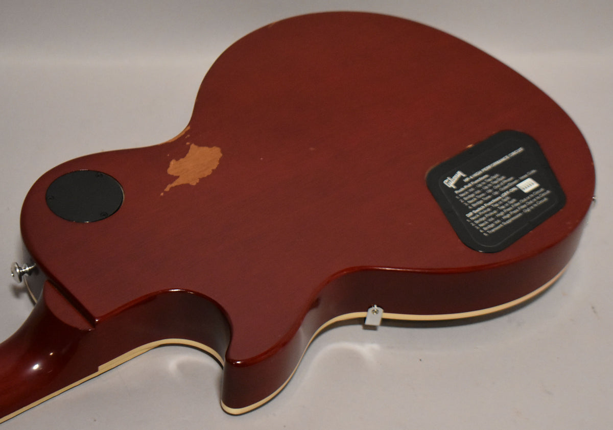 The back of a wine red Les Paul, showing a large area of chipped finish near the upper horn and a black control cavity cover.