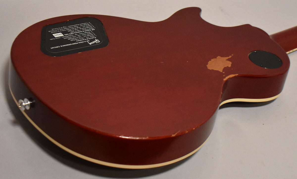 The guitar's wine red back shows significant paint chipping near the cutaway and a black control plate with white text.