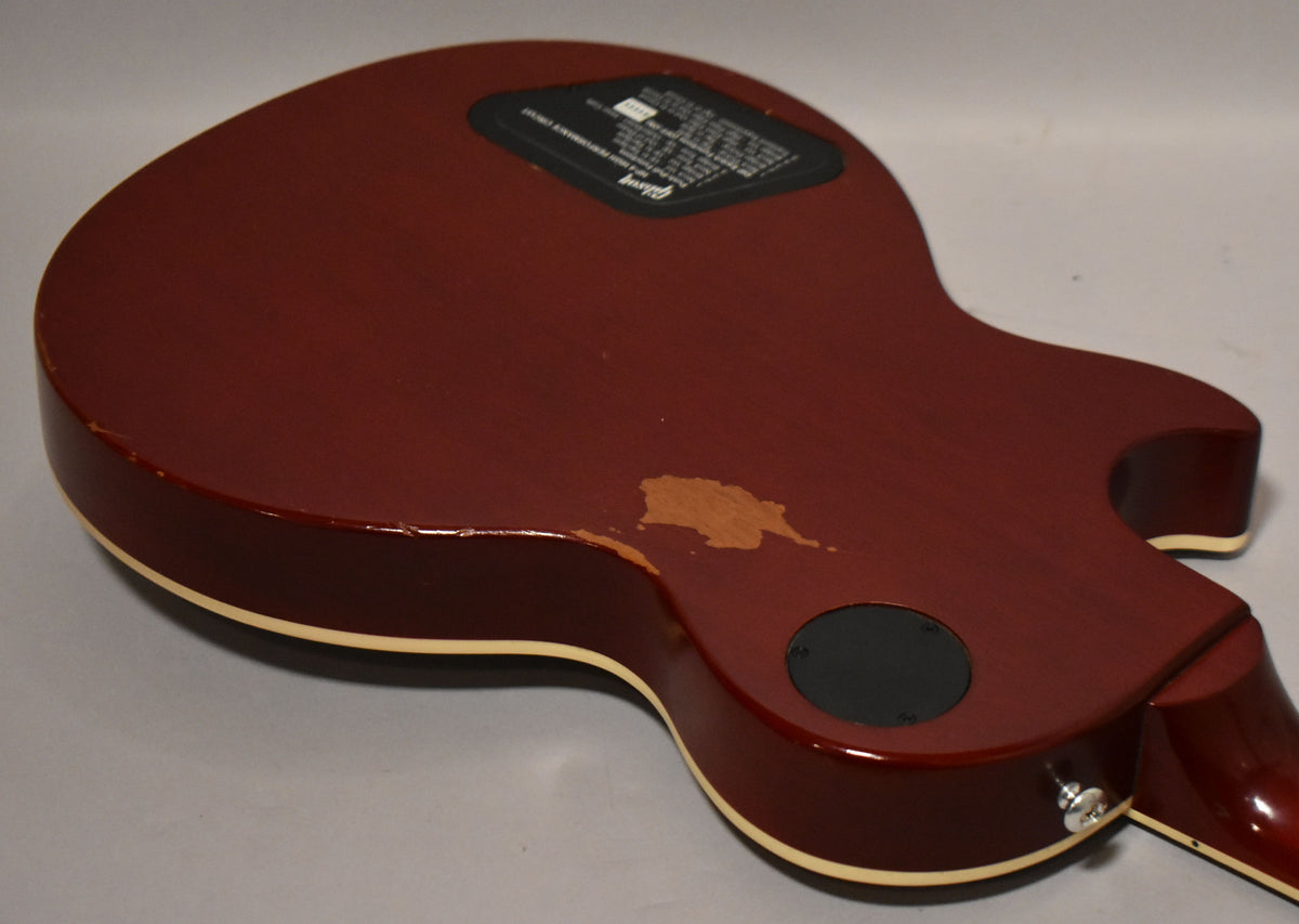 The back of a wine red guitar shows a large area of finish wear, a black control plate, and a chrome output jack.