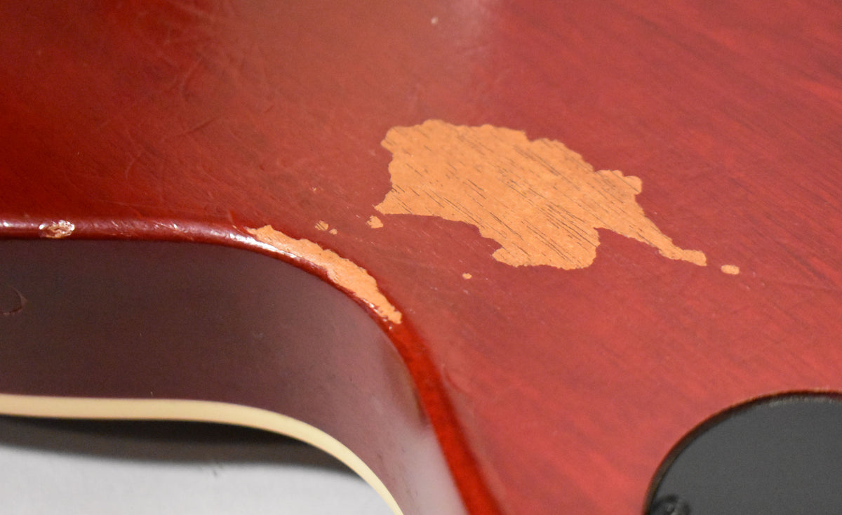 Close-up of the guitar's wine red body, showing significant finish wear and chipping revealing the lighter wood underneath.