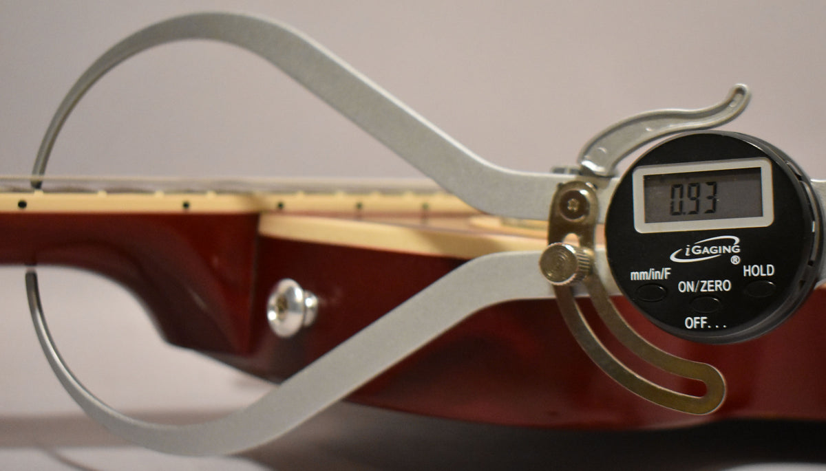 A digital caliper measures the neck thickness of the wine red guitar, displaying 0.93 on its screen.