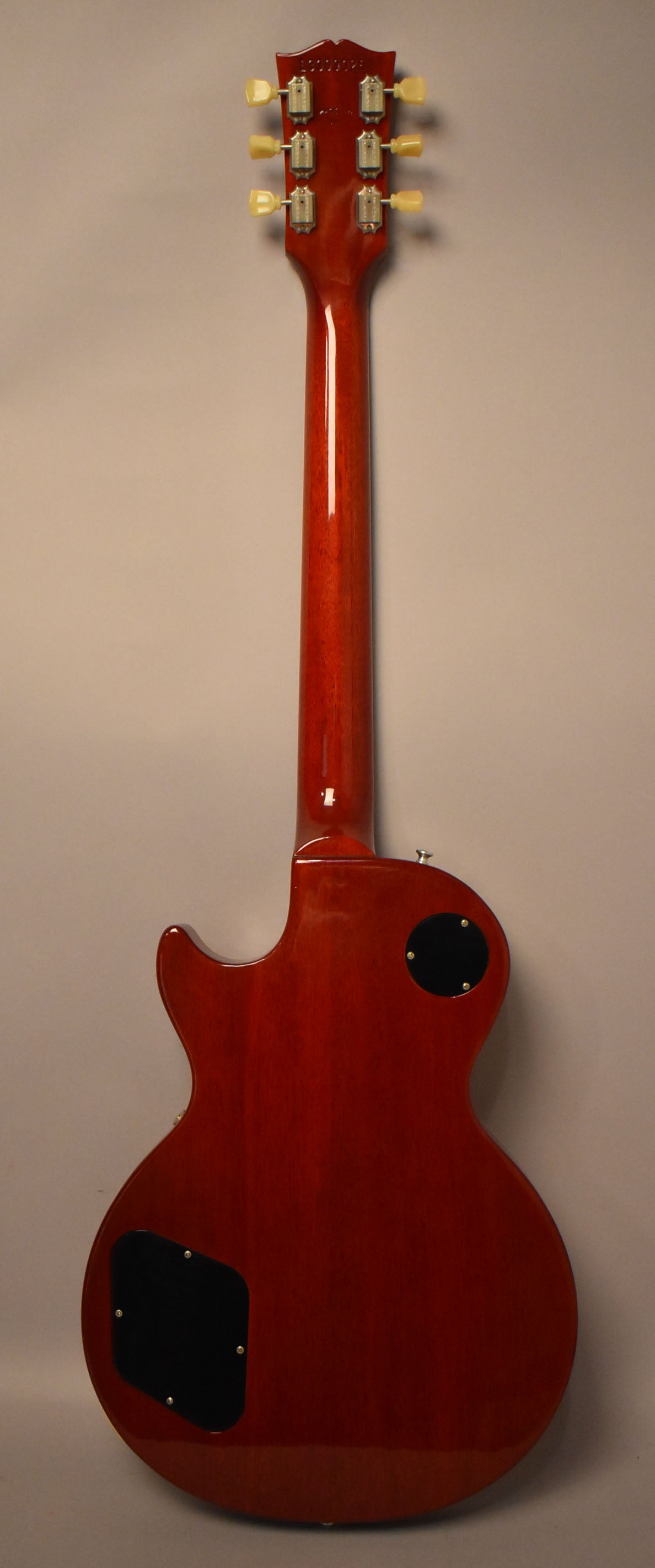 Full rear view of a cherry sunburst Les Paul, showing the headstock with cream tuners, neck, and body with two black control plates.