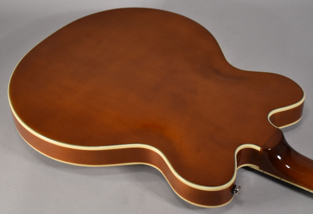 The guitar's sunburst back and sides are visible, with cream binding along the edges and a chrome strap button near the neck heel.