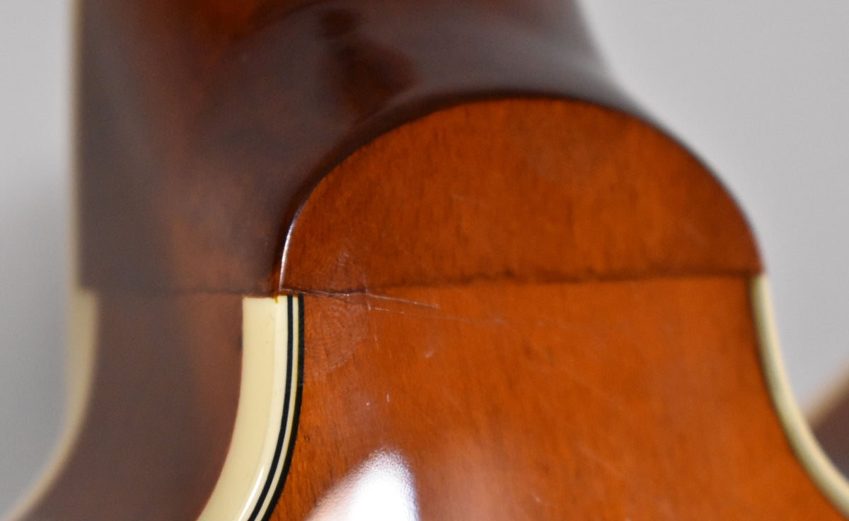 Close-up of the guitar's neck heel and body in sunburst finish, showing light scratches and binding with black pinstripes.