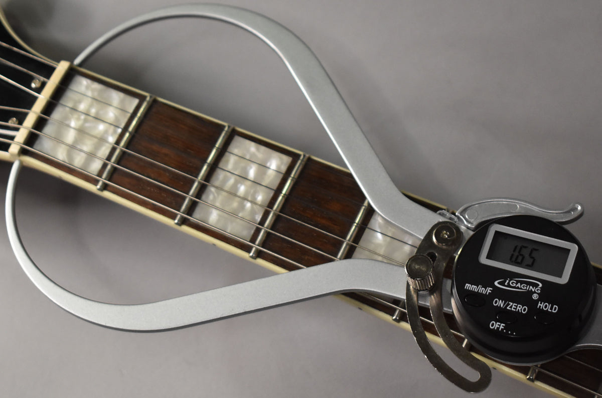 Close-up of the fretboard with block inlays, showing a digital caliper measuring the string height at 1.65mm.