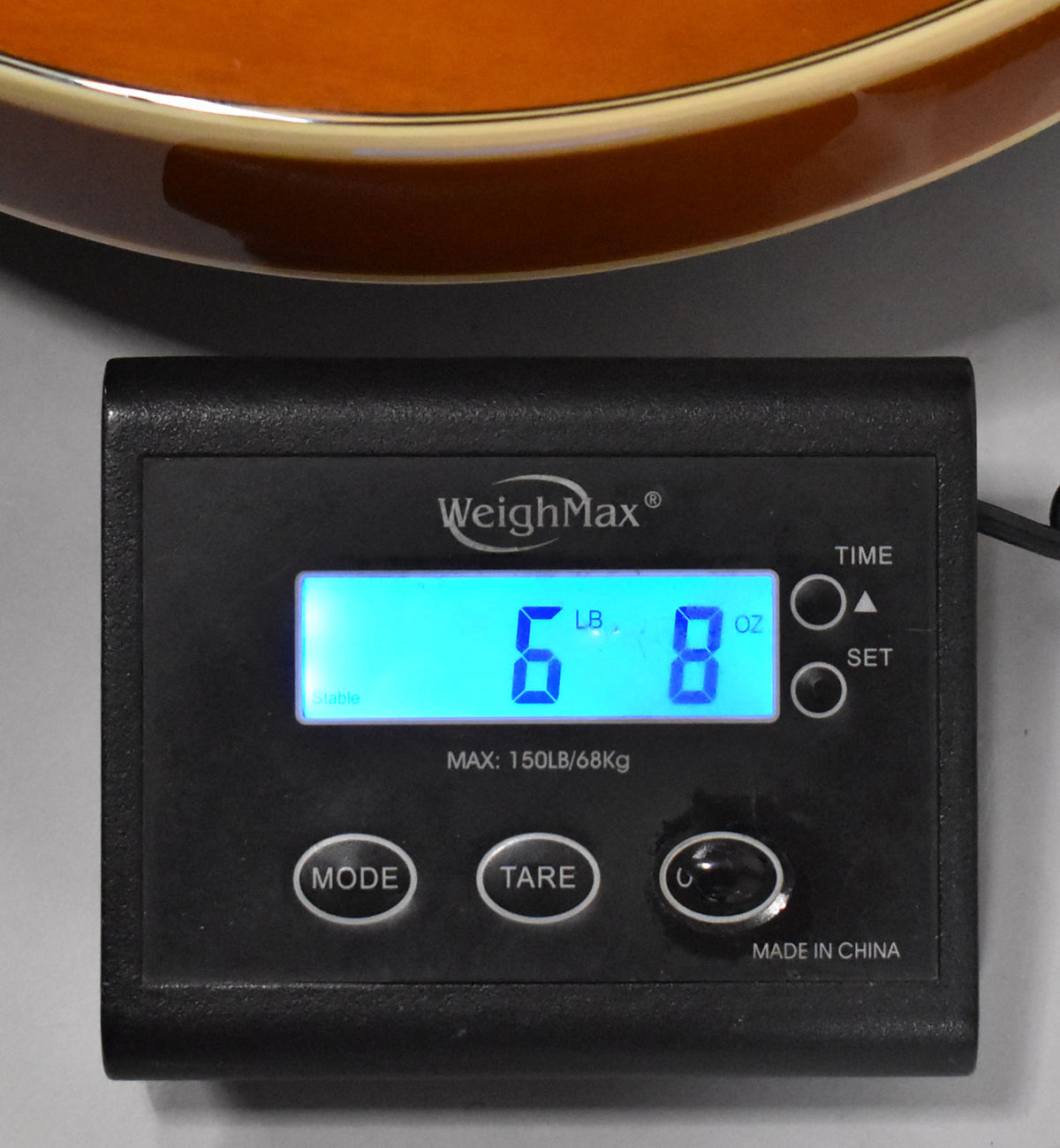 A close-up of a black digital scale showing "6 LB 8 OZ" with the guitar's sunburst body and binding visible at the top.
