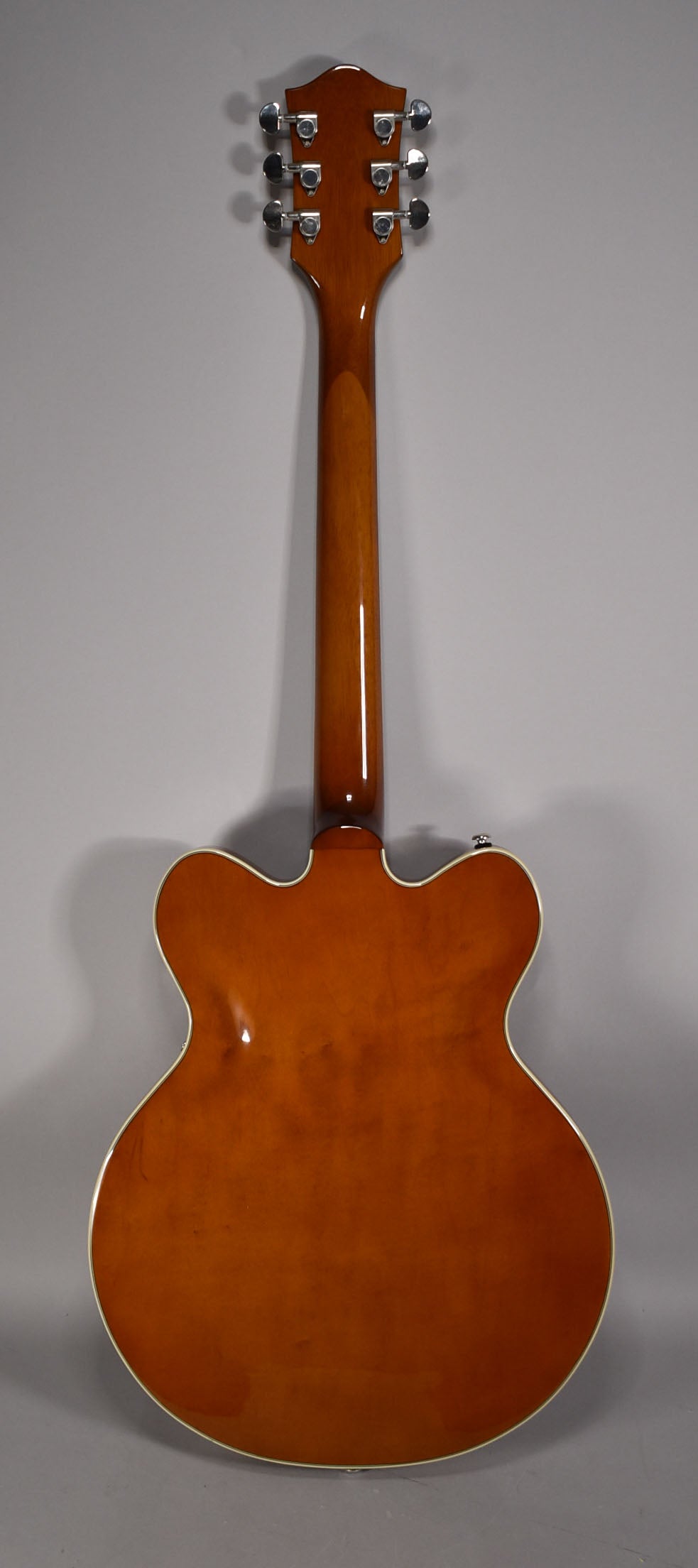 The back of a glossy sunburst semi-hollowbody guitar, showing the neck, headstock with six chrome tuners, and cream binding.