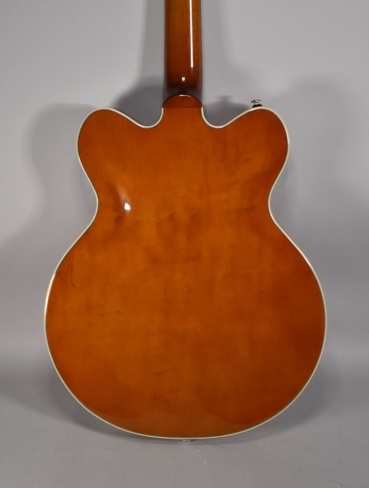 Full back view of a glossy sunburst semi-hollowbody electric guitar with cream binding, showing the neck joint and strap button.