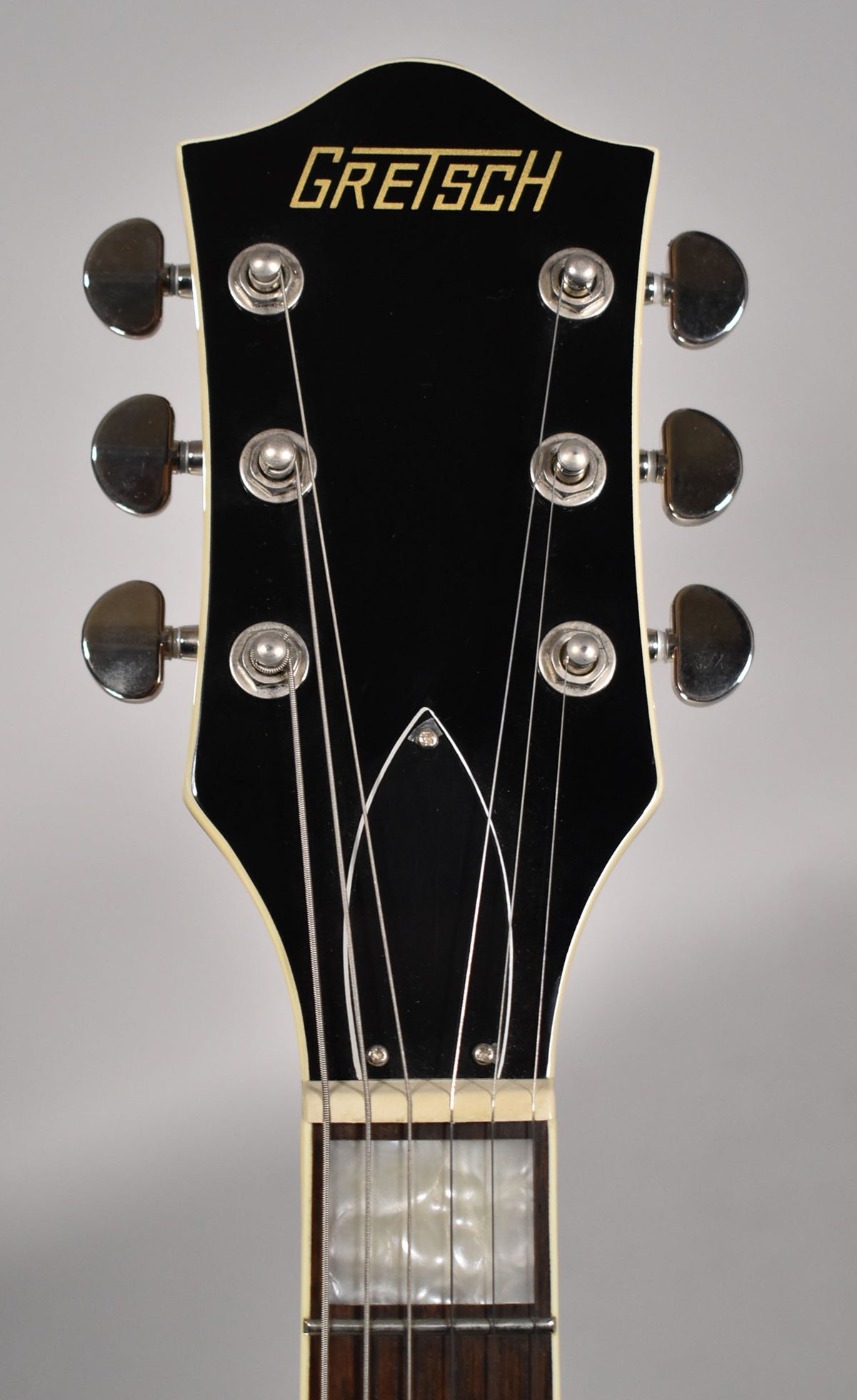 Close-up of the black headstock with gold logo, chrome tuners, and mother-of-pearl block inlay on the dark fretboard.