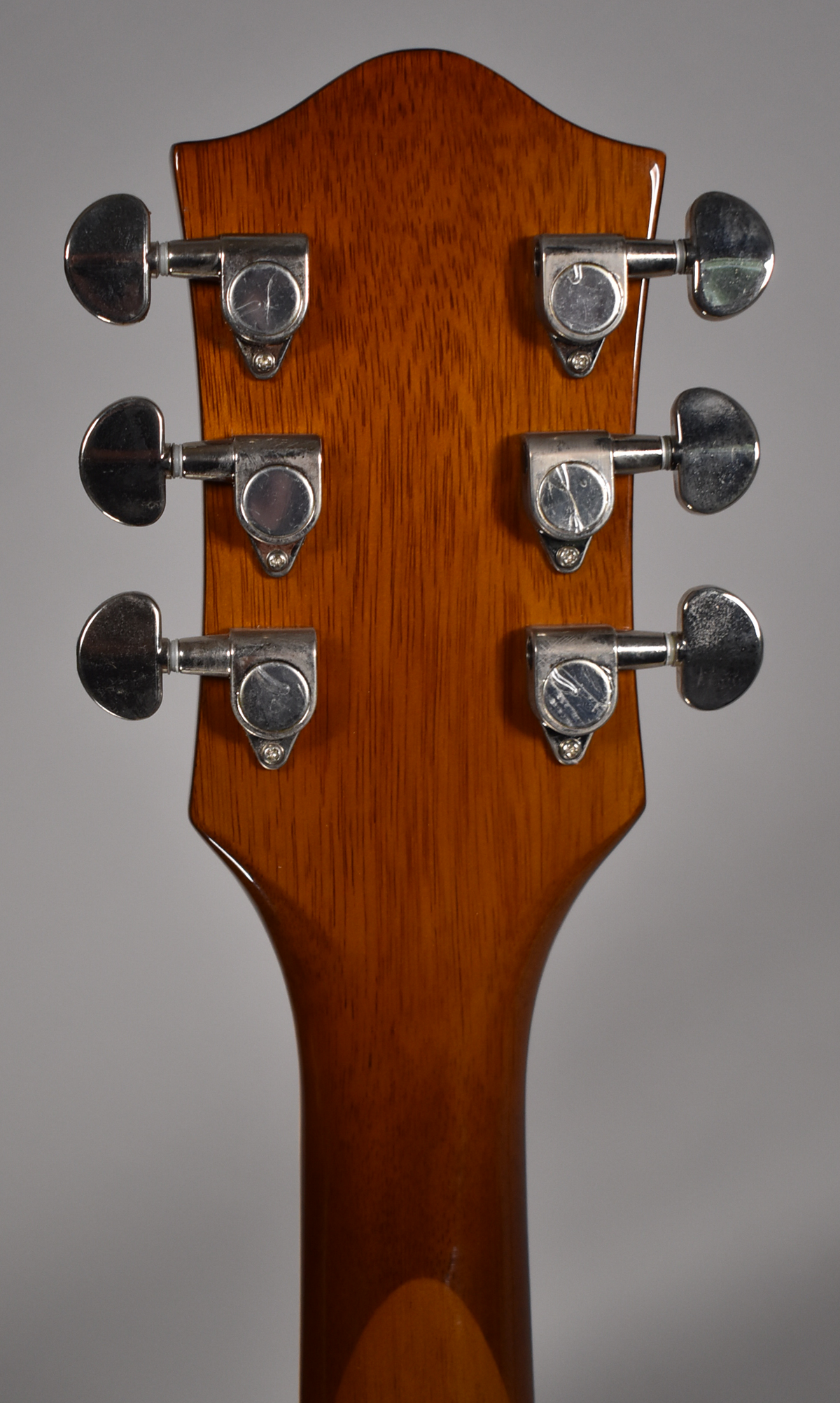 Rear view of the guitar's headstock and upper neck, showing a glossy brown finish and six chrome tuners with minor wear.