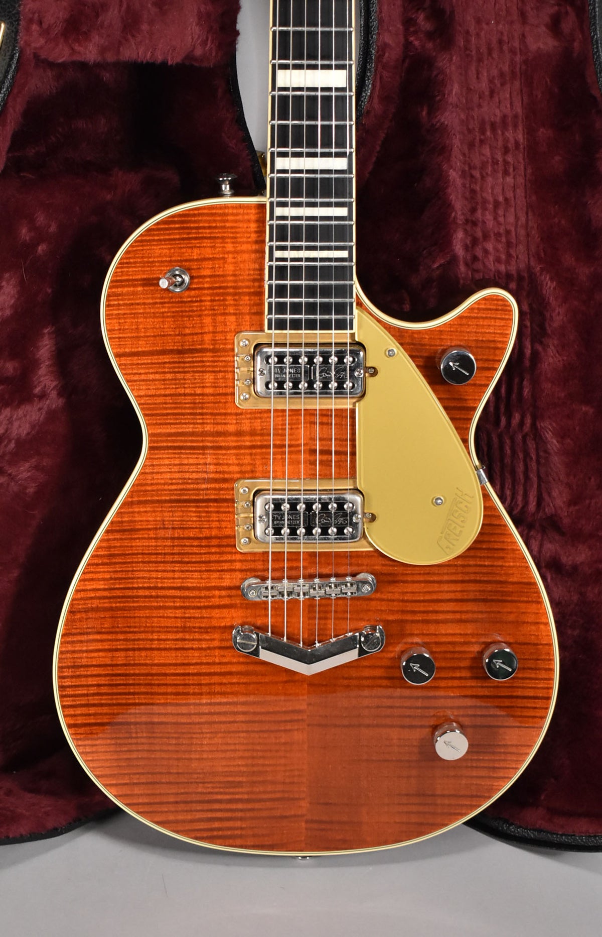 The electric guitar's flame maple body, in a rich orange-brown burst, is centered, showing gold hardware and a cream pickguard.