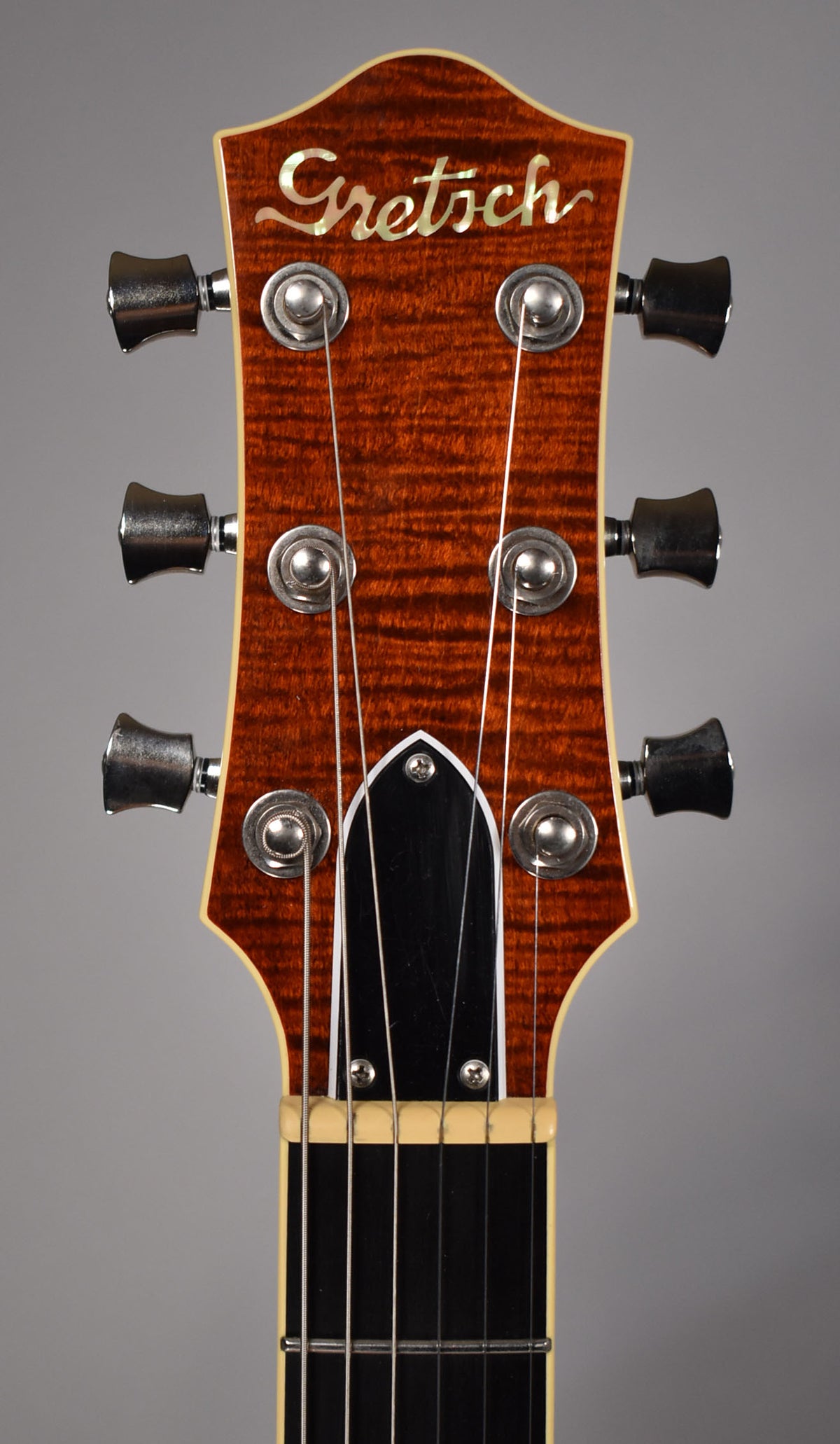 Close-up of the guitar's headstock, showing a flame maple finish, six chrome tuners, and a black truss rod cover.