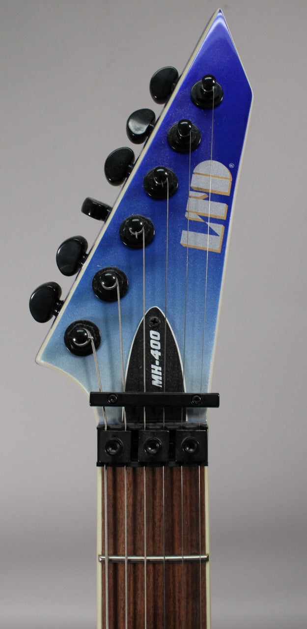 Close-up of the guitar's headstock, showing the blue pearl fade finish, black tuners, and the Floyd Rose locking nut over the dark fretboard.