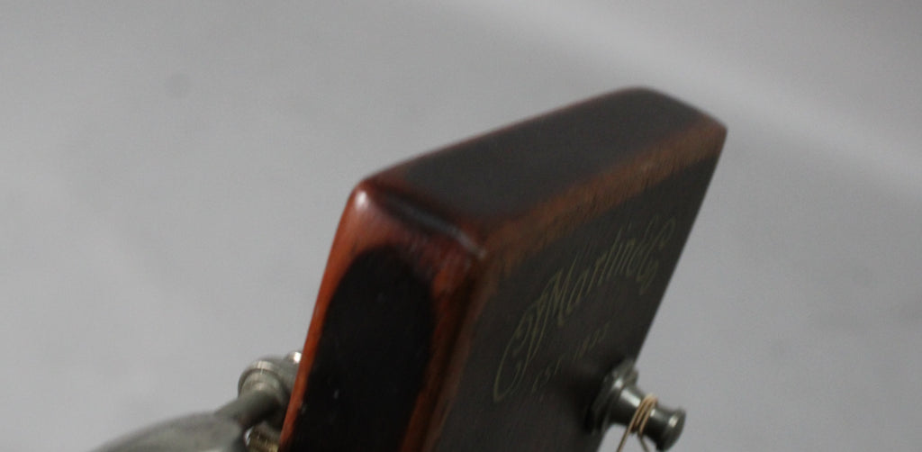 The guitar's dark brown headstock, angled from the left, shows a worn matte finish and a silver tuning peg with a string.