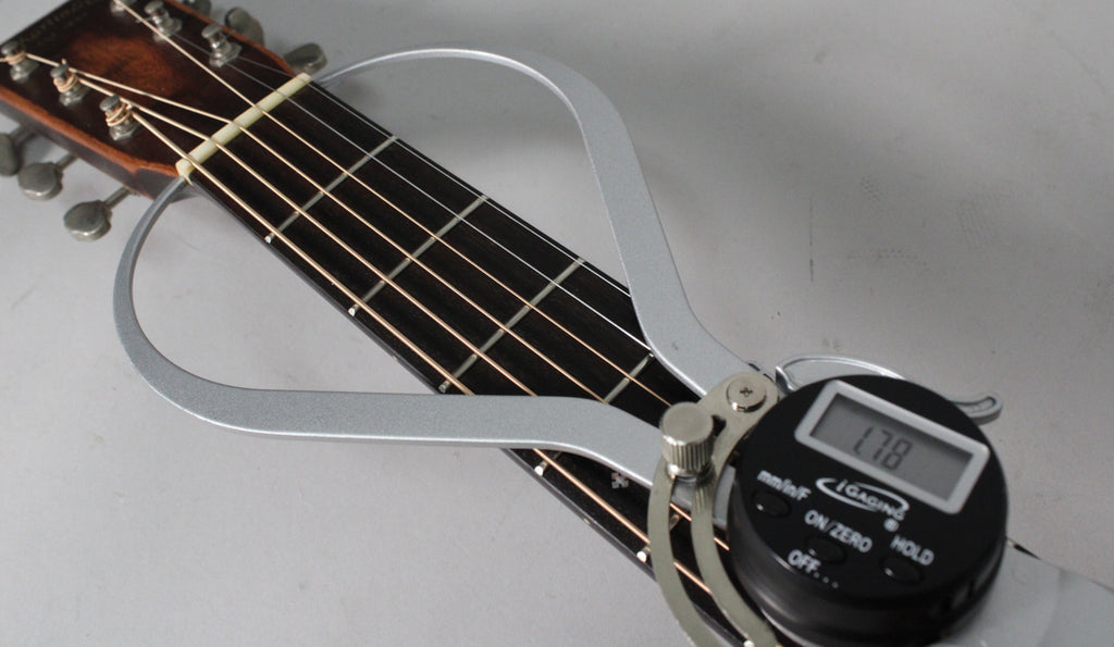 A digital caliper measures the nut width of the dark fretboard and headstock, displaying "1.78" on its screen.