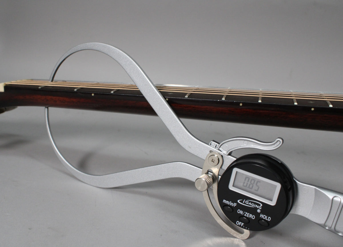 A digital caliper measures the dark brown fretboard and strings, showing a reading of 0.85.