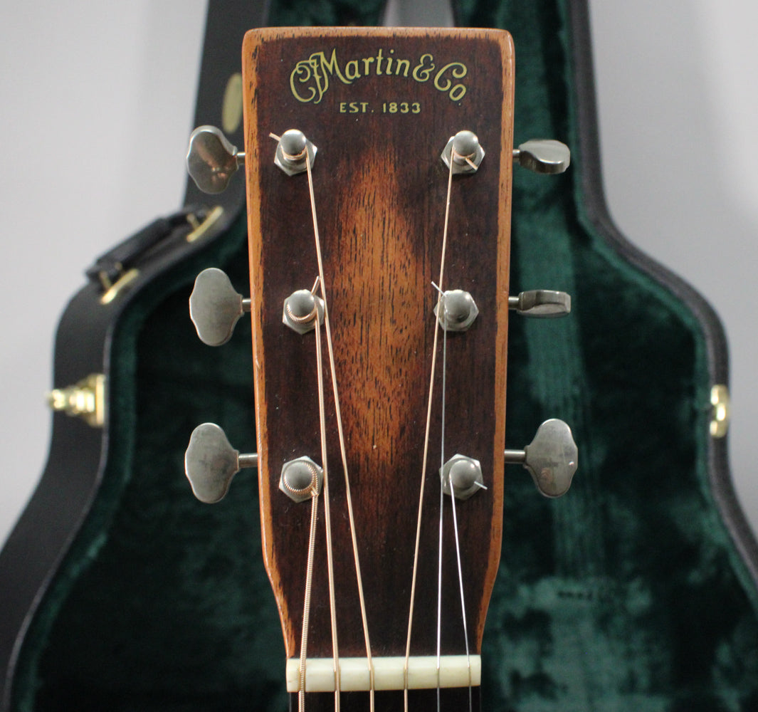 Close-up of the guitar's dark brown headstock with six silver tuners, showing light wear and a green case in the background.