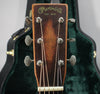Close-up of the guitar's dark brown headstock with six silver tuners, showing light wear and a green case in the background.
