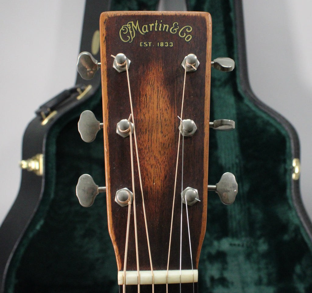 Close-up of the guitar's dark brown headstock with six silver tuners, showing light wear and a green case in the background.