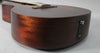The dark brown acoustic guitar's lower bout and endpin jack are visible, with a satin finish and subtle wood grain.