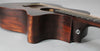 The dark brown acoustic guitar's lower bout and cutaway are visible, with a chrome endpin jack on the heel.
