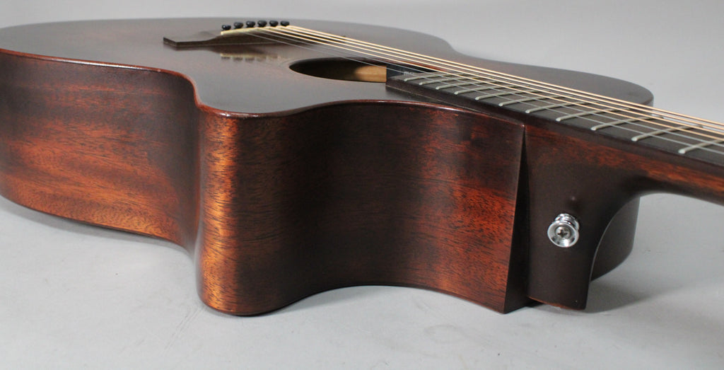 The dark brown acoustic guitar's lower bout and cutaway are visible, with a chrome endpin jack on the heel.