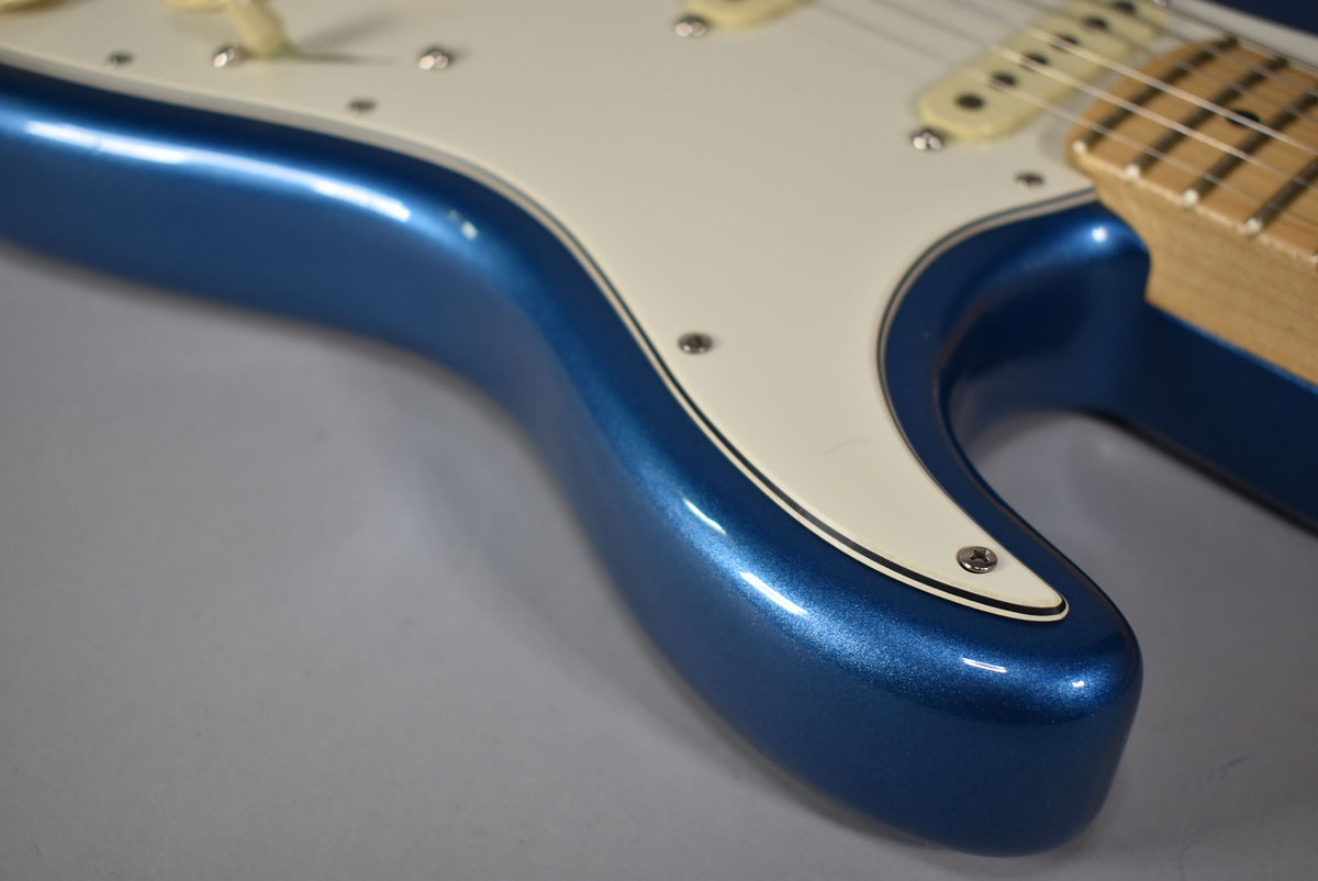 Close-up of the lower bout of a metallic blue Stratocaster, showing the white pickguard with black pinstripe and cream pickups.