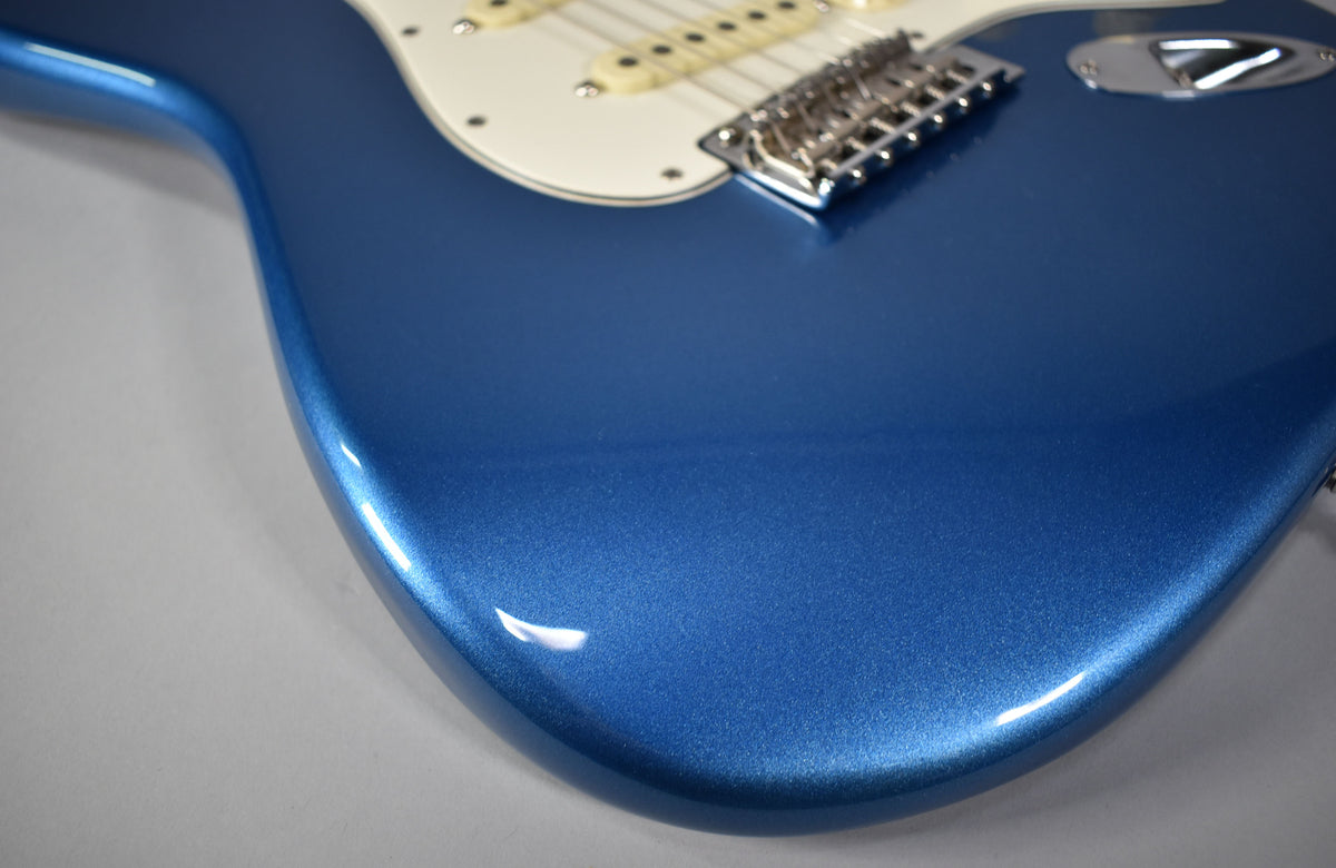 Close-up of the Stratocaster's lower body, showing the metallic blue finish, white pickguard, and chrome bridge.