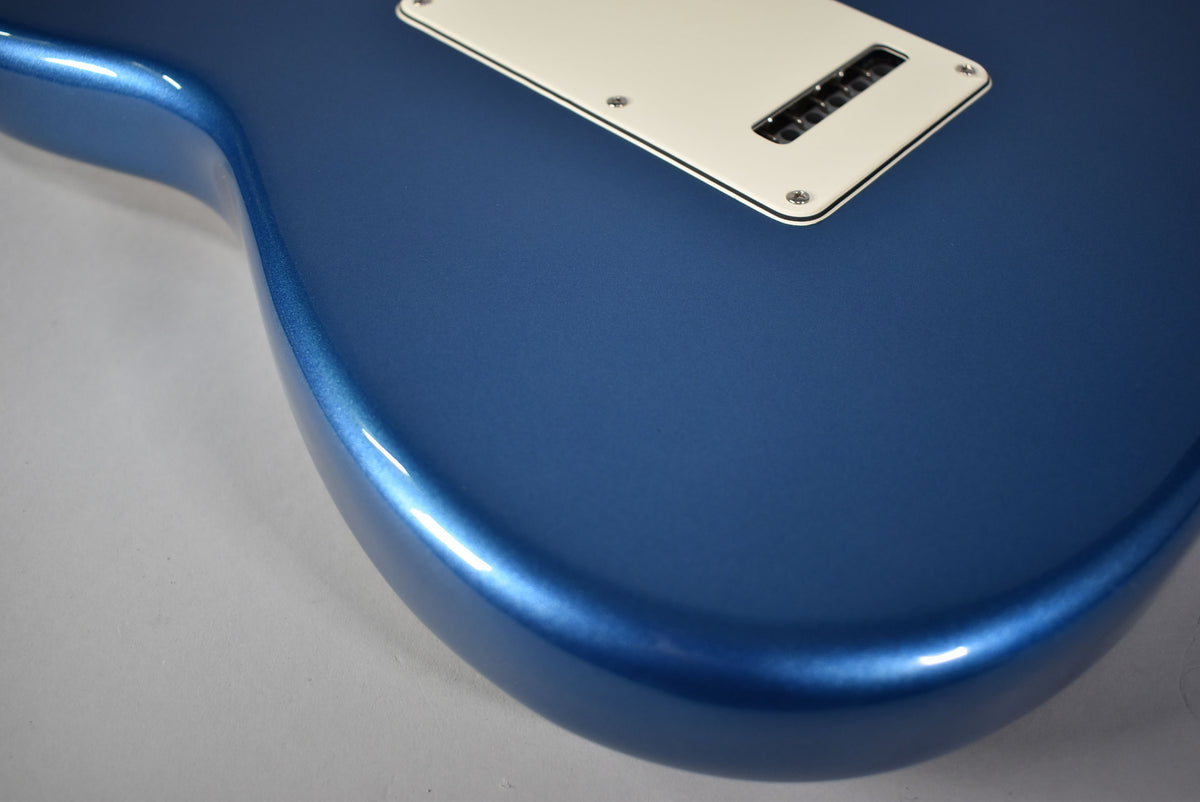 The guitar's lower bout in satin Lake Placid Blue, with a white tremolo cavity cover and six black saddles visible.