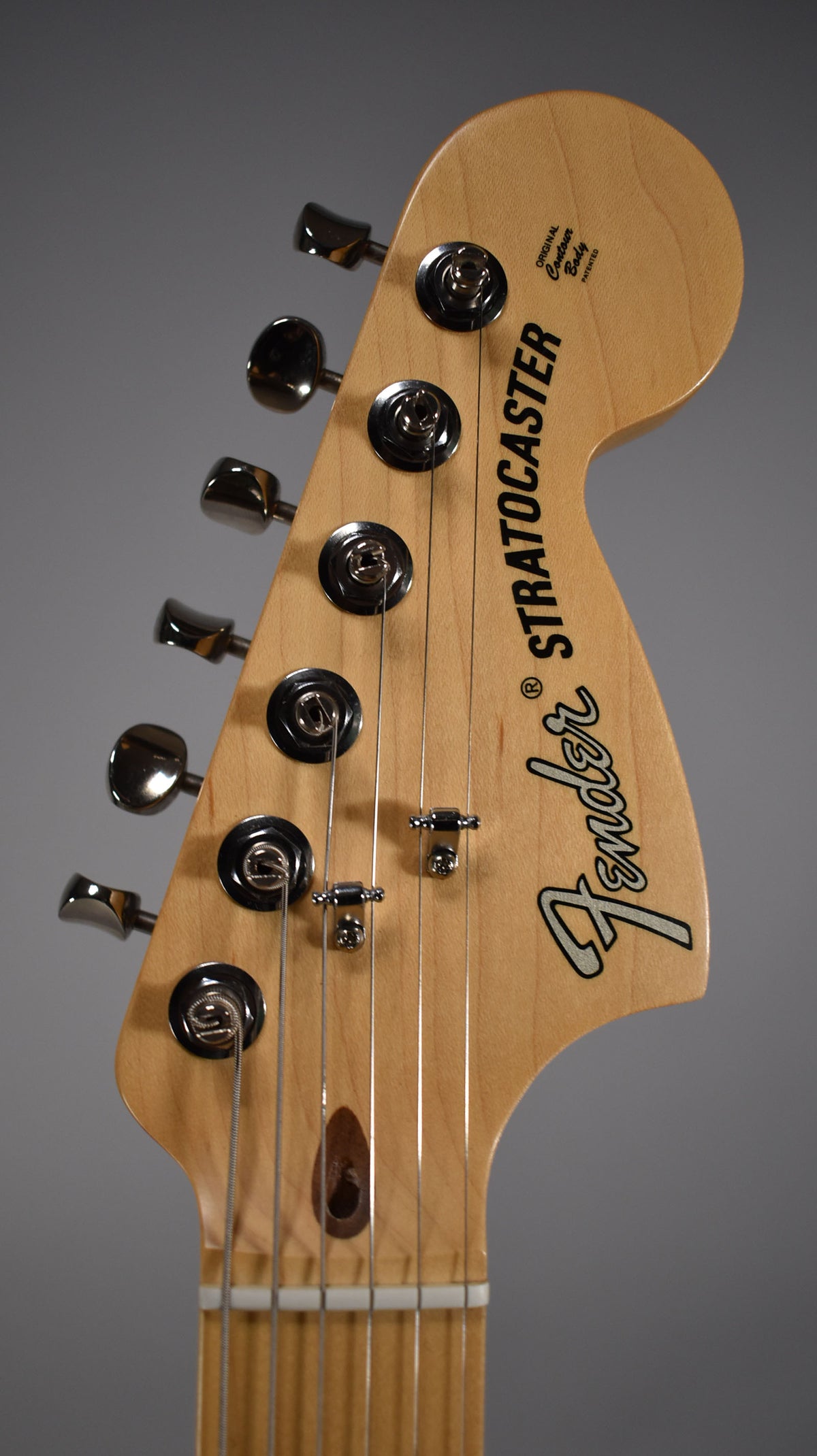 Close-up of the light wood headstock, angled slightly left, showing six chrome tuners, two string trees, and the truss rod access.