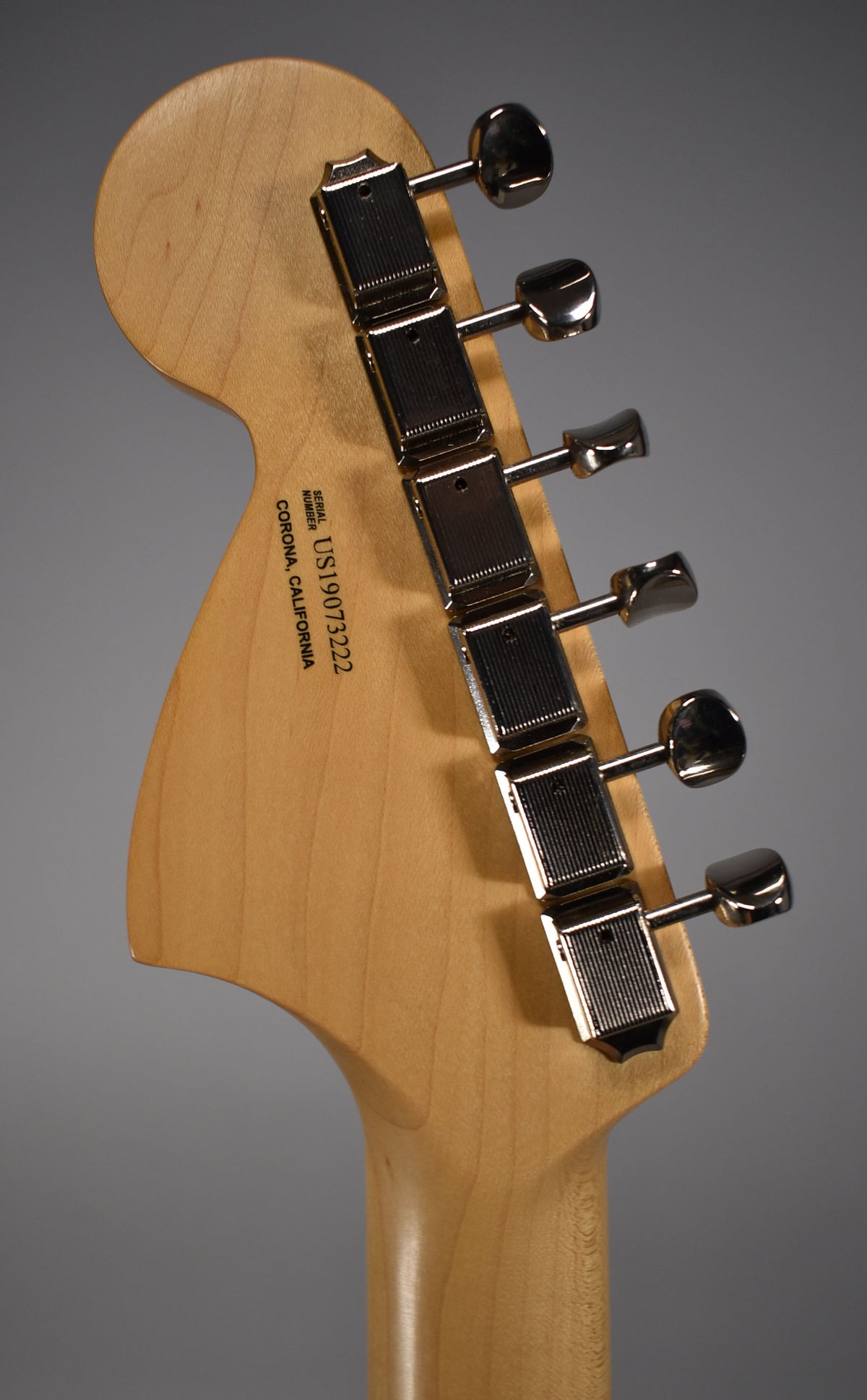 The back of a light wood headstock and neck, angled right, with six chrome tuning machines visible.