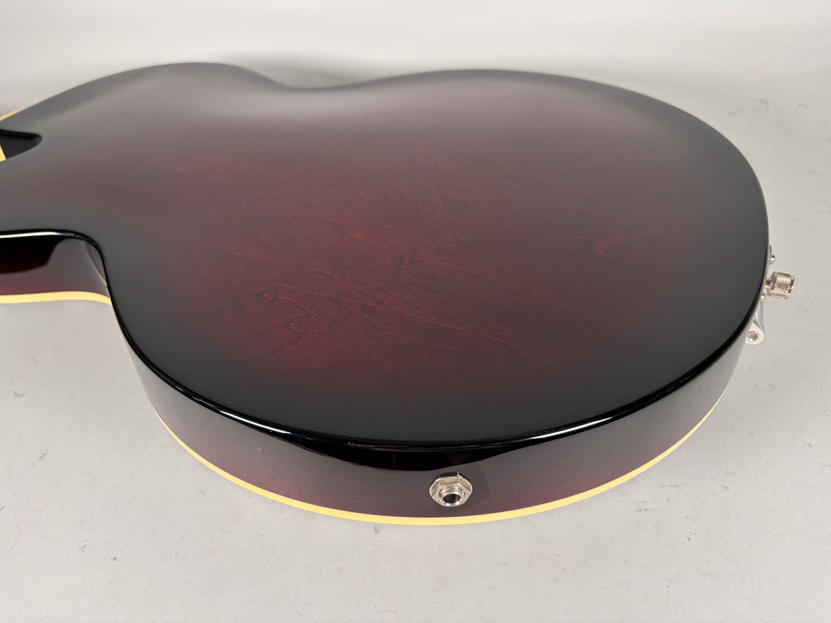 The guitar's dark red back and side are shown, with cream binding, a chrome output jack, and a strap button visible.