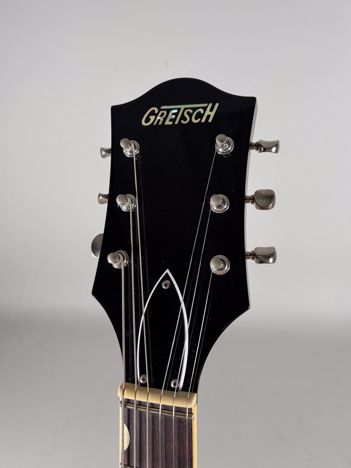Close-up of the glossy black headstock, showing six chrome tuners, a cream nut, and the top of the dark fretboard.