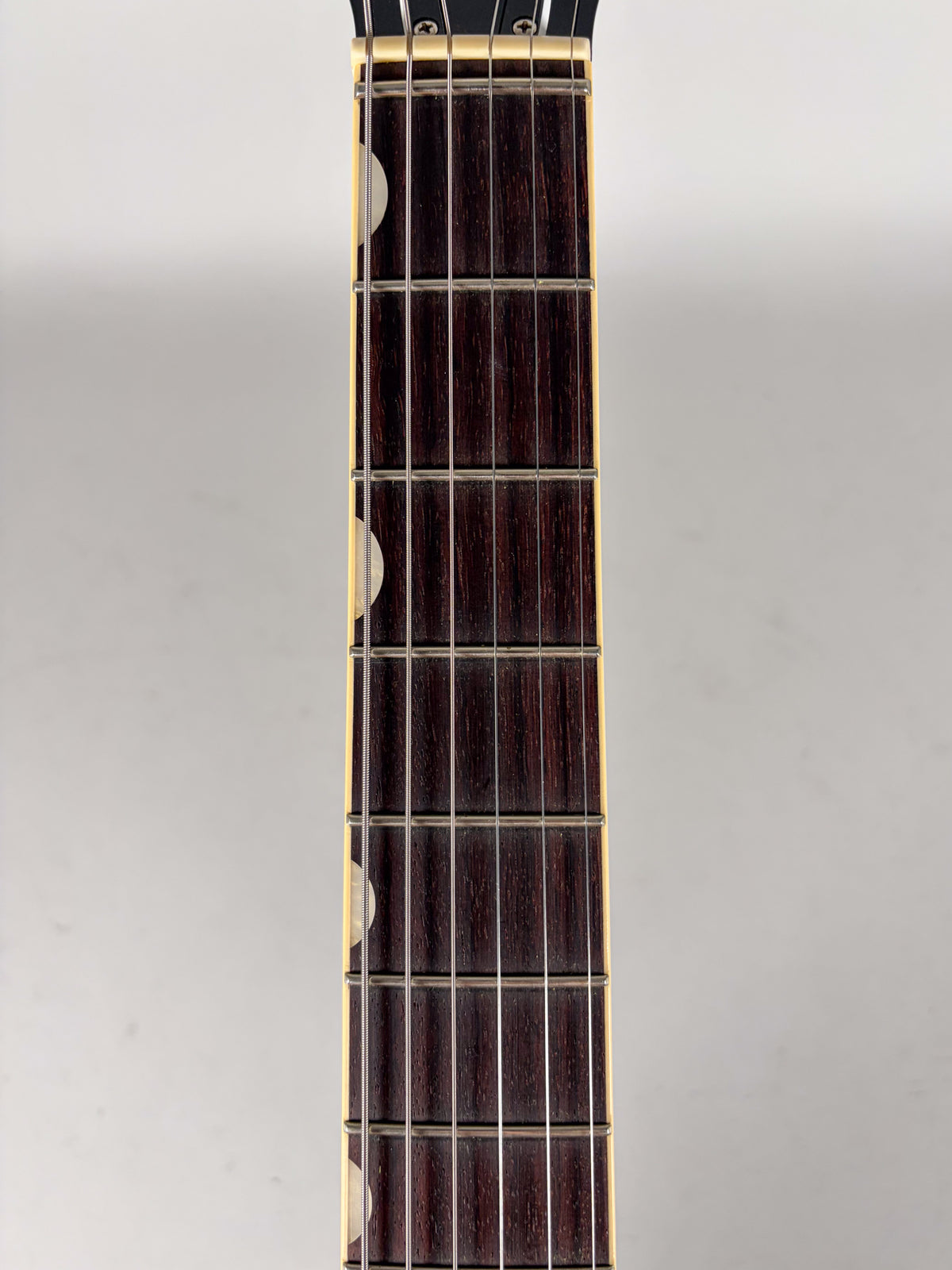 Close-up of the dark rosewood fretboard with six strings, showing cream binding and half-moon pearloid inlays on the bass side.