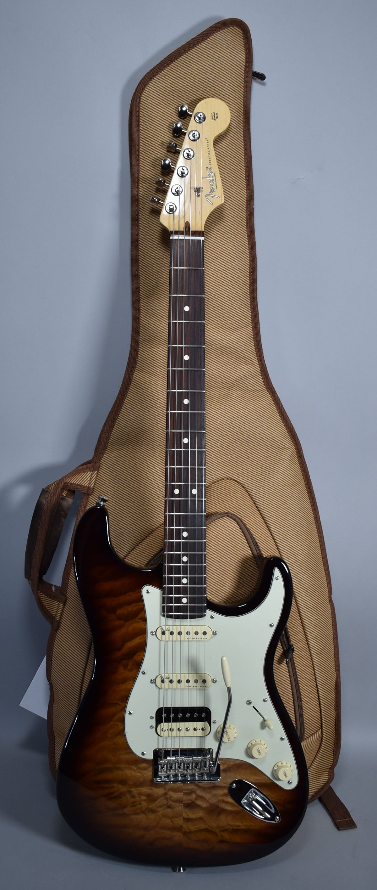 Full-length view of a dark brown burst Stratocaster with a figured maple top, light green pickguard, and humbucker-single-single pickups.