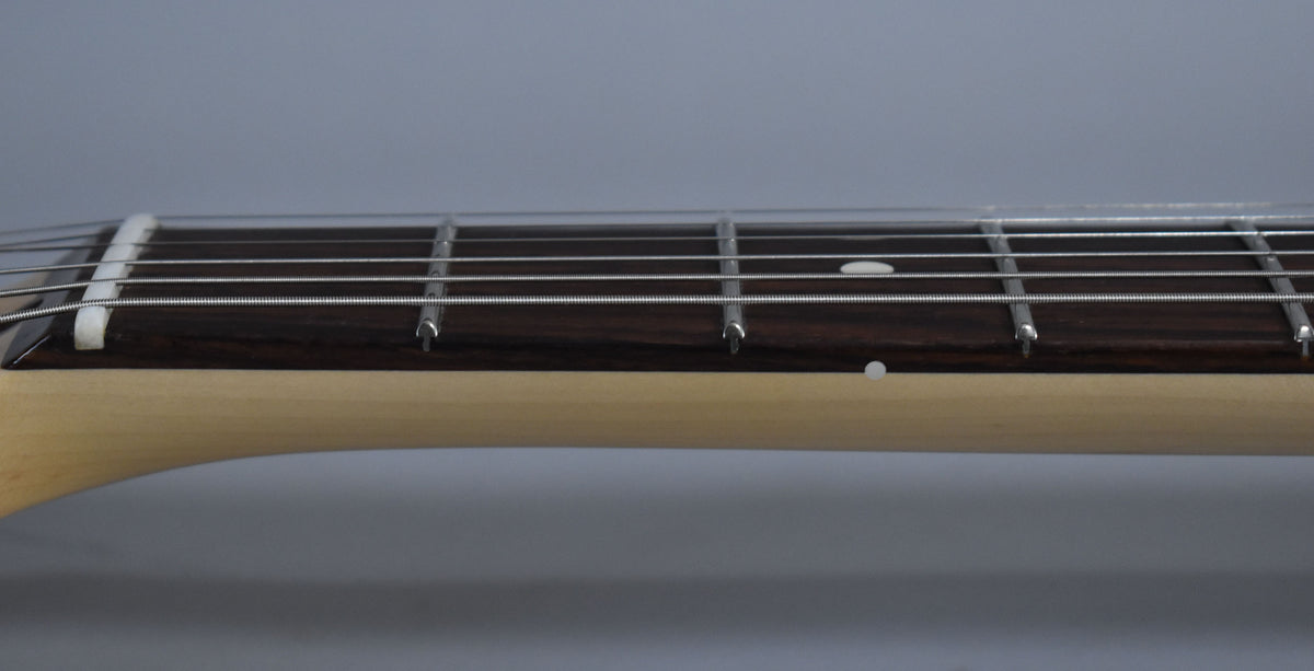 The Stratocaster's dark rosewood fretboard with white dot inlays and a light maple neck is shown from the side, with strings visible.