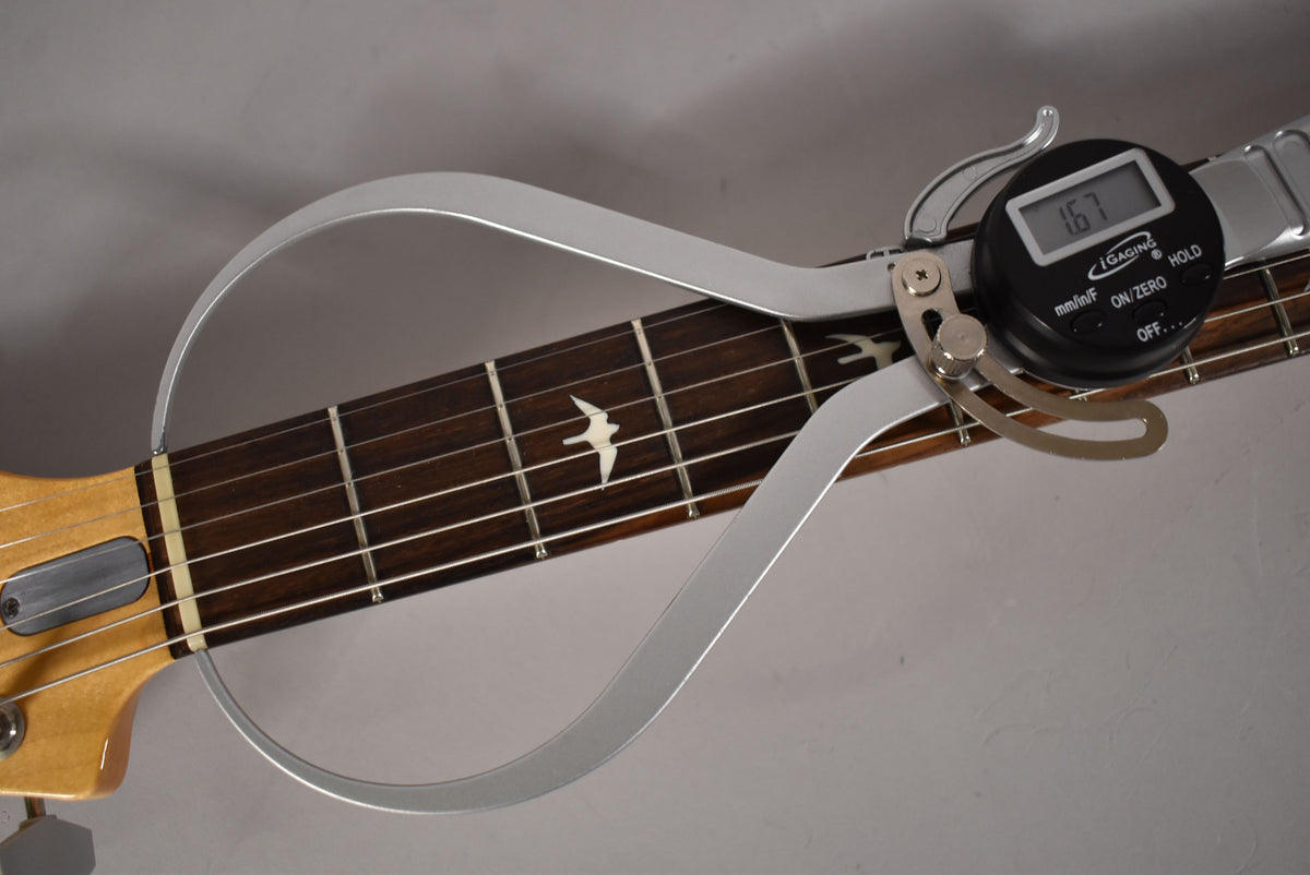 Close-up of the dark rosewood fretboard with bird inlays, showing a digital fret height gauge measuring 1.67mm on the upper frets.