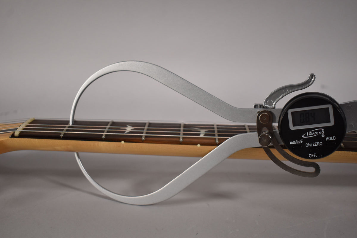 A digital fret rocker tool measures the guitar's dark fretboard and light maple neck, displaying "0.84".